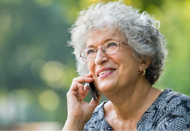 An older woman with grey hair and glasses, talking on the phone