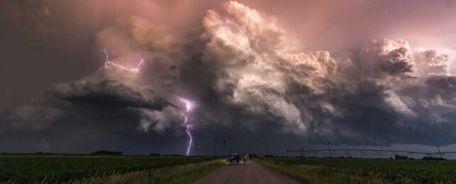 A lightning strike in front of a huge dark cloud above a road