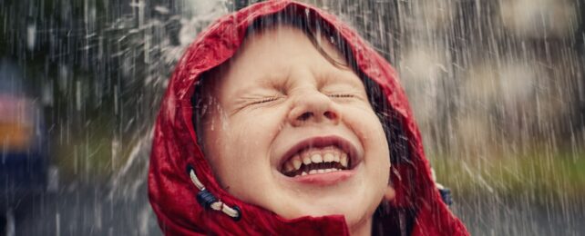 A young child's face wearing a red rain jacket in the rain