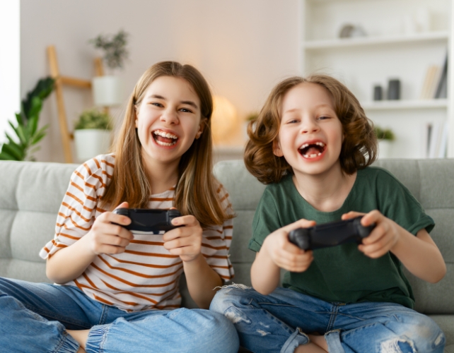 Two laughing kids on a couch with game controllers in their hands