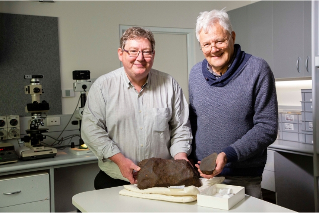 Two men in a museum holding a large rock 