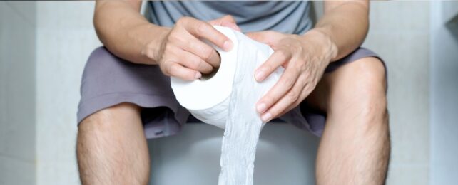 A person sitting on a toilet holding a toilet roll