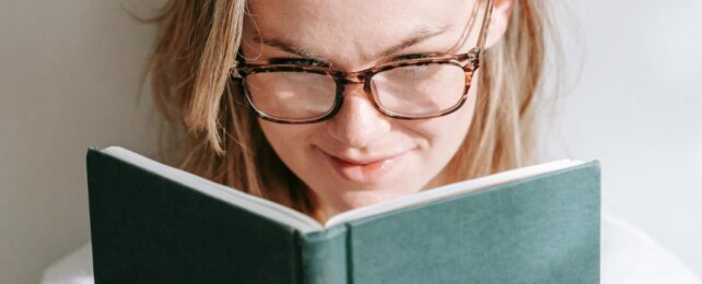 Person with blonde hair and glasses reading a book