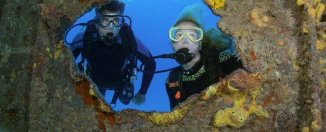 Two scuba divers peering through hole in shipwreck